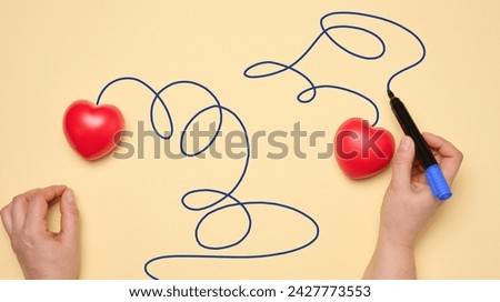 Two red hearts on a yellow background, a woman's hand draws a trajectory, top view