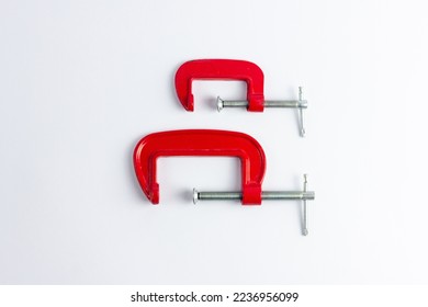 Two red metal clamps of different sizes on a white background. Tools for repair work and DIY projects. Construction, craft, work with wood products.