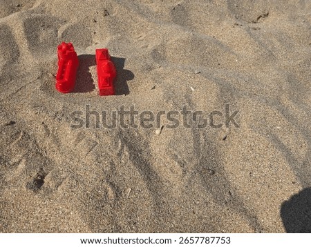 Two red plastic molds shaped like castles placed on sandy beach. Summer toys for children’s playtime by the sea. Minimal composition in bright daylight.