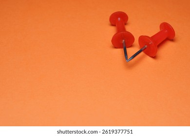 Two red push pins form a V on bright orange paper.