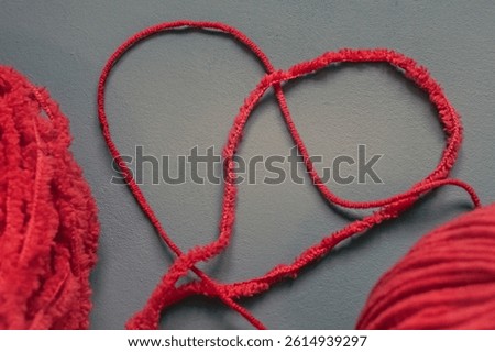 Two red threads in a heart shape. Yarn skeins. Red yarn. Heart shape. Red and gray. Craft maker. Knitted style. Knit or crochet. Word or symbol made of yarn. Needlework as a meditative experience. 