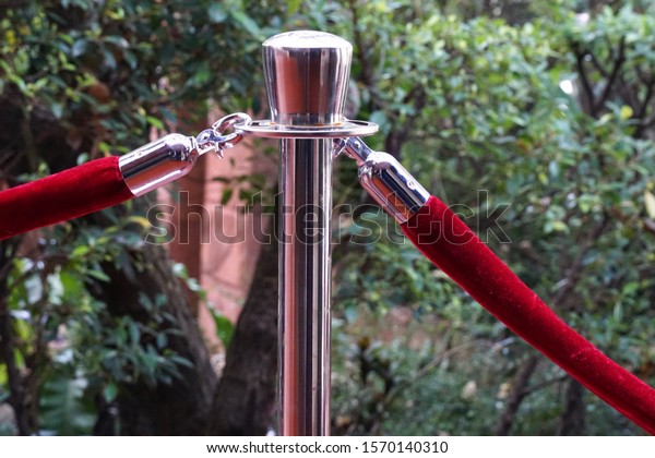 Two red velvet ropes with hookers\
 hanging to stainless pole , trees are blurred\
background.