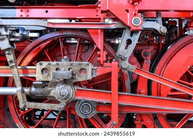 Two red wheels of an old steam locomotive with drive linkage in close-up
