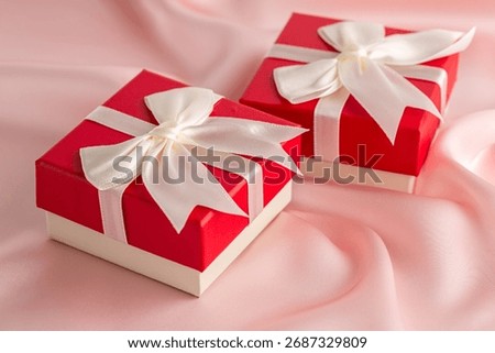 Two red and white gift boxes with ribbon on the pink silk background.