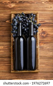 Two Red Wine Bottles Composition On Brown Wooden Table. Red Wine Bottles In Box On Black Ripe Grapes On Wooden Table. Old Collection Wine Label Template Top View Vertical