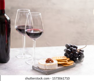 Two Red Wine Glasses And Charcuterie Board With Different Snacks For Wine. French Cheese, Grapes And Crackers. 