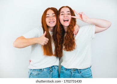 two redheaded young women both looking happy one shows like sign another victory sign standing on isolated white backgroung