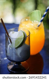 Two refreshing summer drinks on a table, one with orange juice and the other with lime and whipped cream. High quality photo
