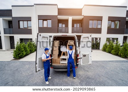 Two removal company workers are loading boxes and furniture into a minibus.