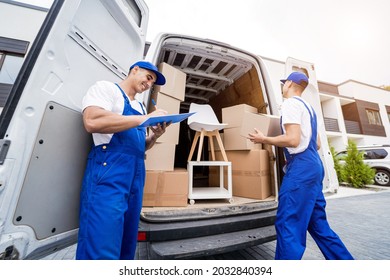 Two Removal Company Workers Unloading Boxes And Furniture From Minibus