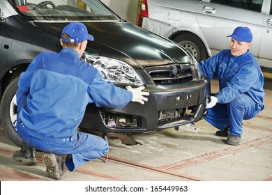 Two repairman mechanics matching automobile body bumper on damaged car at repair service station