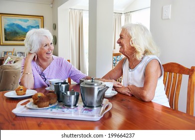 Two Retired Older Women Sitting Together Having Tea And Muffins And Laughing