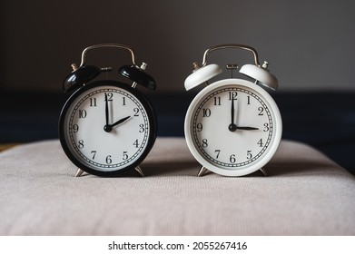 Two retro table clocks, black and white color, showing daylight saving time concept - Shutterstock ID 2055267416