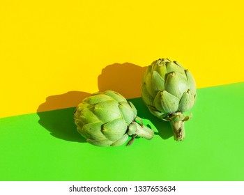 Two Ripe Artichokes On Duotone Yellow Green Background. Hard Light Harsh Shadows. Trendy Funky Minimalist Style. Creative Food Poster Banner. Healthy Plant Based Diet Mediterranean Cuisine. Copy Space