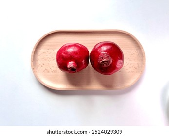 Two ripe pomegranates resting on a rustic wooden board. Their vibrant red color and textured skin showcase the fruit's natural beauty, perfect for food photography and culinary use. - Powered by Shutterstock