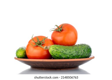 Two ripe tomatoes and two cucumbers on a clay plate, macro, isolated on a white background.