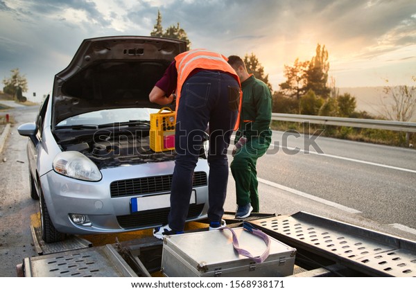 Two road assistant workers in towing\
service trying to start car engine with jump starter and energy\
station with air compressor. Roadside assistance\
concept.