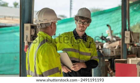 Two robotic technicians in high visibility jackets and hard hats discuss operations in an industrial setting, emphasizing collaboration and safety in robotics maintenance facility and management.