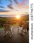 Two rocking chairs on a balcony overlooking a beautiful sunrise with focus on front of chair and railing