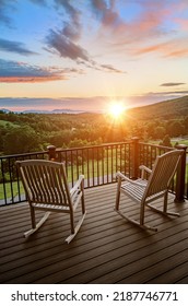 Two rocking chairs on a balcony overlooking a beautiful sunrise with focus on front of chair and railing
