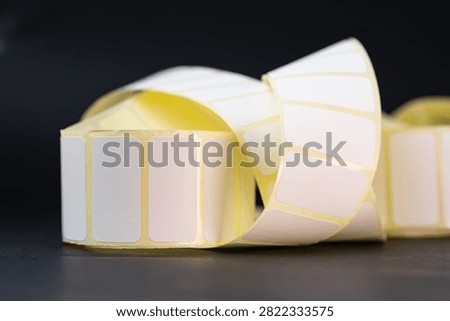 Two rolls of blank white adhesive labels with curled strips on a black studio surface.