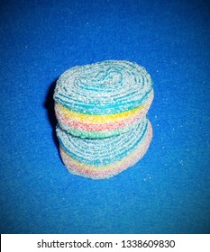 Two Rolls Of Rainbow Sour Tape Candy Stacked On A Blue Background