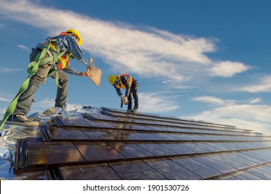 Two roofers Wearing safety clothing is working as a team to install the roof of the house that Ceramic tile roof at construction site