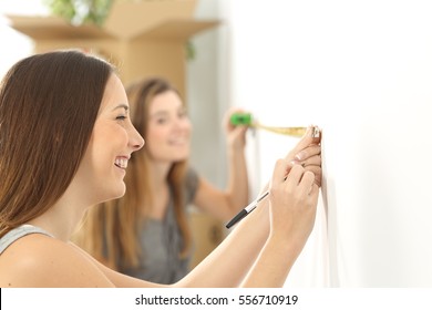 Two roommates measuring with a measure tape in a wall helping each other while they are moving home - Powered by Shutterstock