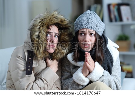 Two roommates shivering in a cold winter day on a couch in the living room at home 