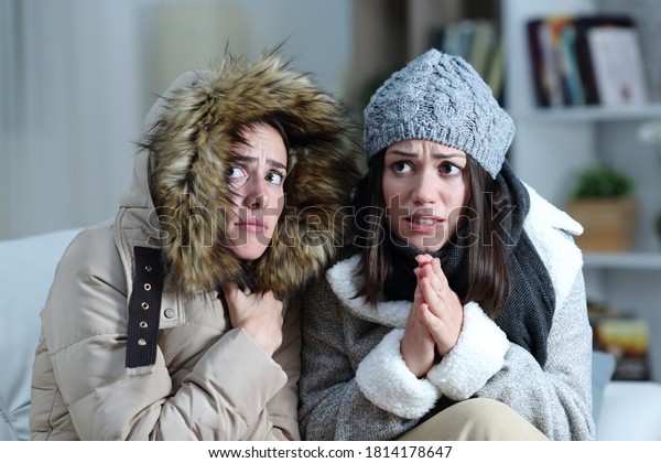 Two roommates shivering in a cold winter\
day on a couch in the living room at home\
