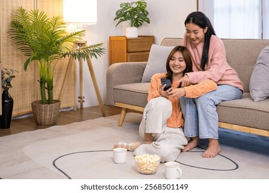 Two roommates using their mobile phones on line at home sitting on a sofa in the living room at home.Happy roommates checking their smart phones.