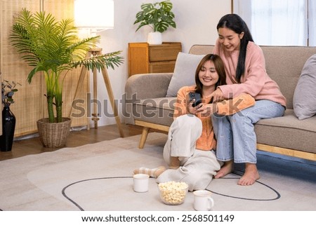 Two roommates using their mobile phones on line at home sitting on a sofa in the living room at home.Happy roommates checking their smart phones.