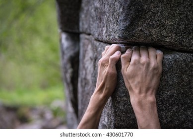 Two rough hands with taped fingers gripping a rock ledge during a bouldering.