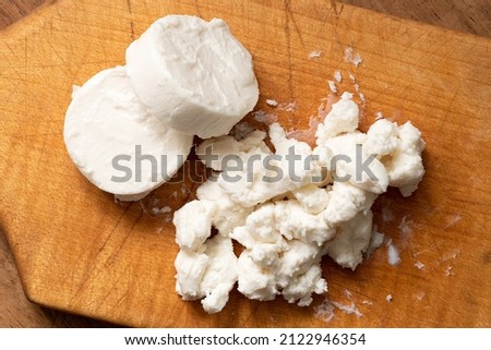 Two rounds of goat cheese and crumbled goat cheese on wood chopping board. Top view.