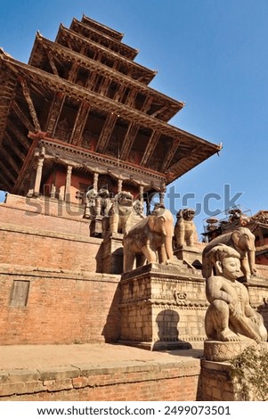 Two rows of big stone statues, sculptures, guardians line up next to the stairs leading up to the Nyatapola Temple with its elaborate wooden roof construction, Bhaktapur, Nepal 2022