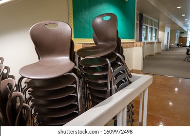 Two rows of brown stacking chairs at a school setting piled under some stairs