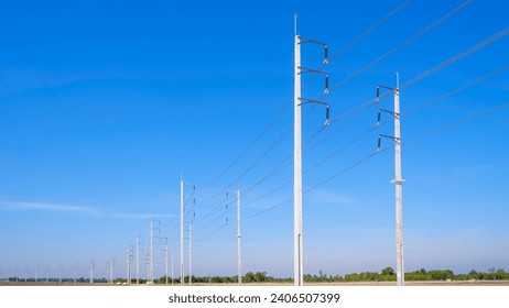 Two rows of electric poles with cable lines on curve country road against blue sky background, low angle and perspective side view