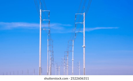 Two rows of electric poles with cable lines on curve country road against blue sky background, low angle view with copy space