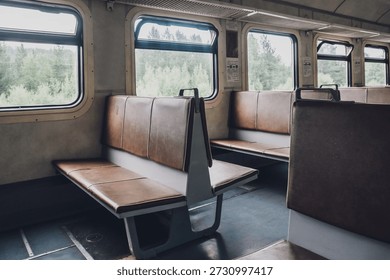 two rows empty benches sit in train car. windows show green landscape outside. scene captures moment during journey. close up.