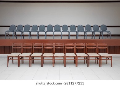 Two rows of neat, elegant chairs in a spacious, pristine, yet empty room, arranged in two rows. One row is positioned on top of a raised pulpit platform, while the other is situated directly below at its foot. One row is a sleek slate gray, and the other is a warm coffee-and-cream brown.