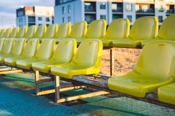 Two Rows Of Plastic Yellow Outdoor Stadium Seats. Objects Are Worn Out, Dirty And Aged. Rusted Metal Holding Construction Is Under Seats. One Seat Is Missing Out Of The Row (selective Focus).