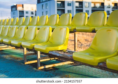 Two Rows Of Plastic Yellow Outdoor Stadium Seats. Objects Are Worn Out, Dirty And Aged. Rusted Metal Holding Construction Is Under Seats. One Seat Is Missing Out Of The Row (selective Focus).