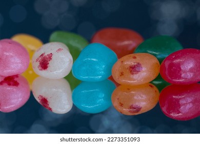 Two rows of soft candy jelly beans colourfully reflected in a mirror.  The red, blue orange, yellow and green beans are set against a black sparkly background.