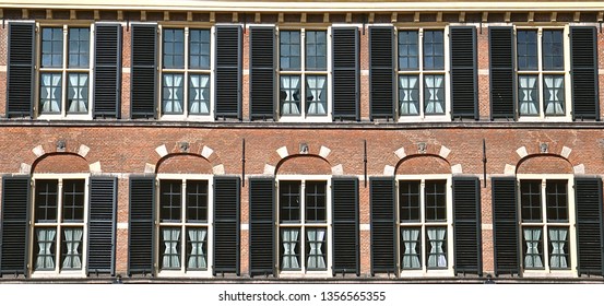 Two rows of windows with lead lights and black wooden louvred shutters. 