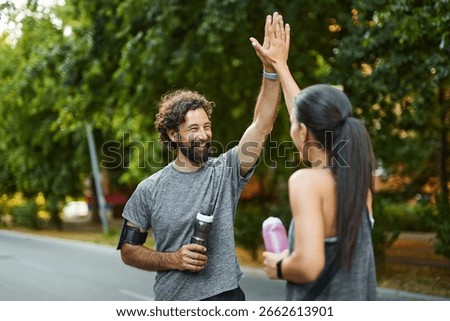Two runners share a joyous high-five after completing part of their route in a park on a sunny morning, showcasing the joy of fitness and friendship in outdoor activities.