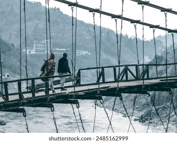 Two rural persons crossing a serene lake on a rustic wooden bridge, surrounded by lush greenery and tranquil waters. The bridge stretches across the lake,creating connection between the two mountains. - Powered by Shutterstock