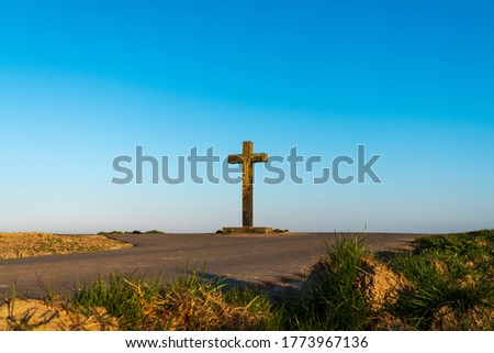 Two rural roads intersect at a big old Christian stone cross in front of a clear blue sky at the beginning sunset. Concept of Christian belief, being at the crossroads, making a decision