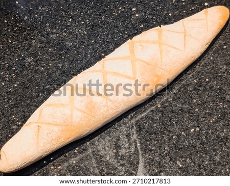 Two rustic loaves of artisan bread displayed side by side on a dark textured surface, showcasing distinct scoring styles—one with diagonal slashes and the other with a crisscross pattern.