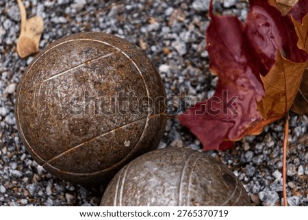 Two rusty boule balls by a leaf in the gravel