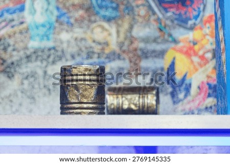 Two rusty metal cans placed on a white shelf with a vibrant and colorful blurred background featuring various shapes and patterns.